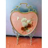 FRENCH BRASS HEART SHAPED FIRESCREEN WITH A BEVELLED MIRROR PAINTED WITH FLOWERS ON FOUR SCROLL FEET