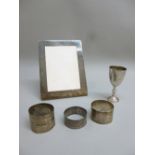 A SILVER PHOTOGRAPH FRAME (12.8 cm x 16.5 cm), THREE SILVER NAPKIN RINGS AND A SMALL SILVER CUP (