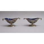 A PAIR OF EDWARDIAN SILVER PIERCED AND EMBOSSED BOOT-SHAPED PEDESTAL SALT CELLARS WITH BLUE GLASS