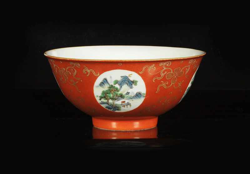 A red porcelain medallion bowl with a polychrome decor of several landscapes and gold colored floral