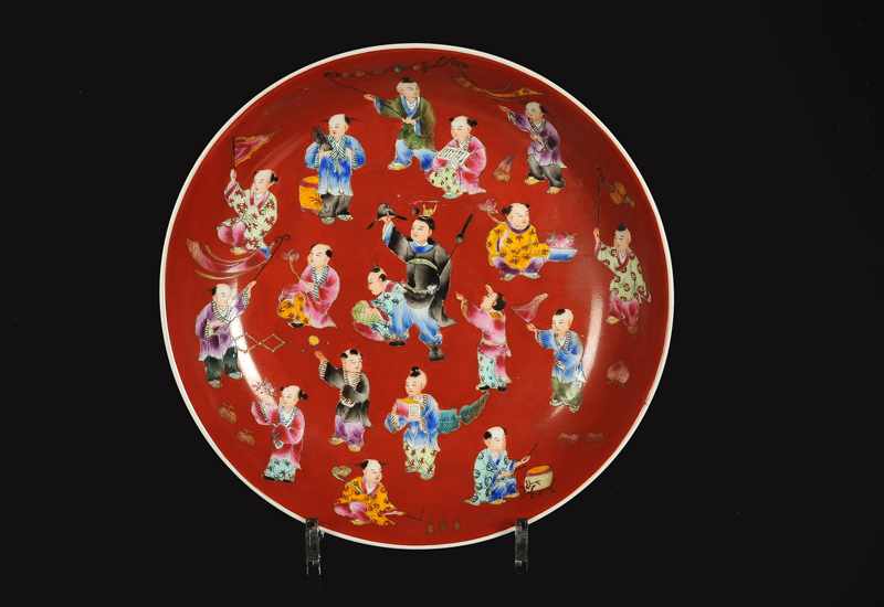 A red porcelain dish with a polychrome decor of boys with attributes. Marked with seal mark