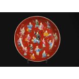 A red porcelain dish with a polychrome decor of boys with attributes. Marked with seal mark