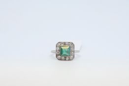 An Emerald and diamond ring. The square cut emerald with old cut diamond surround. Mount stamped '