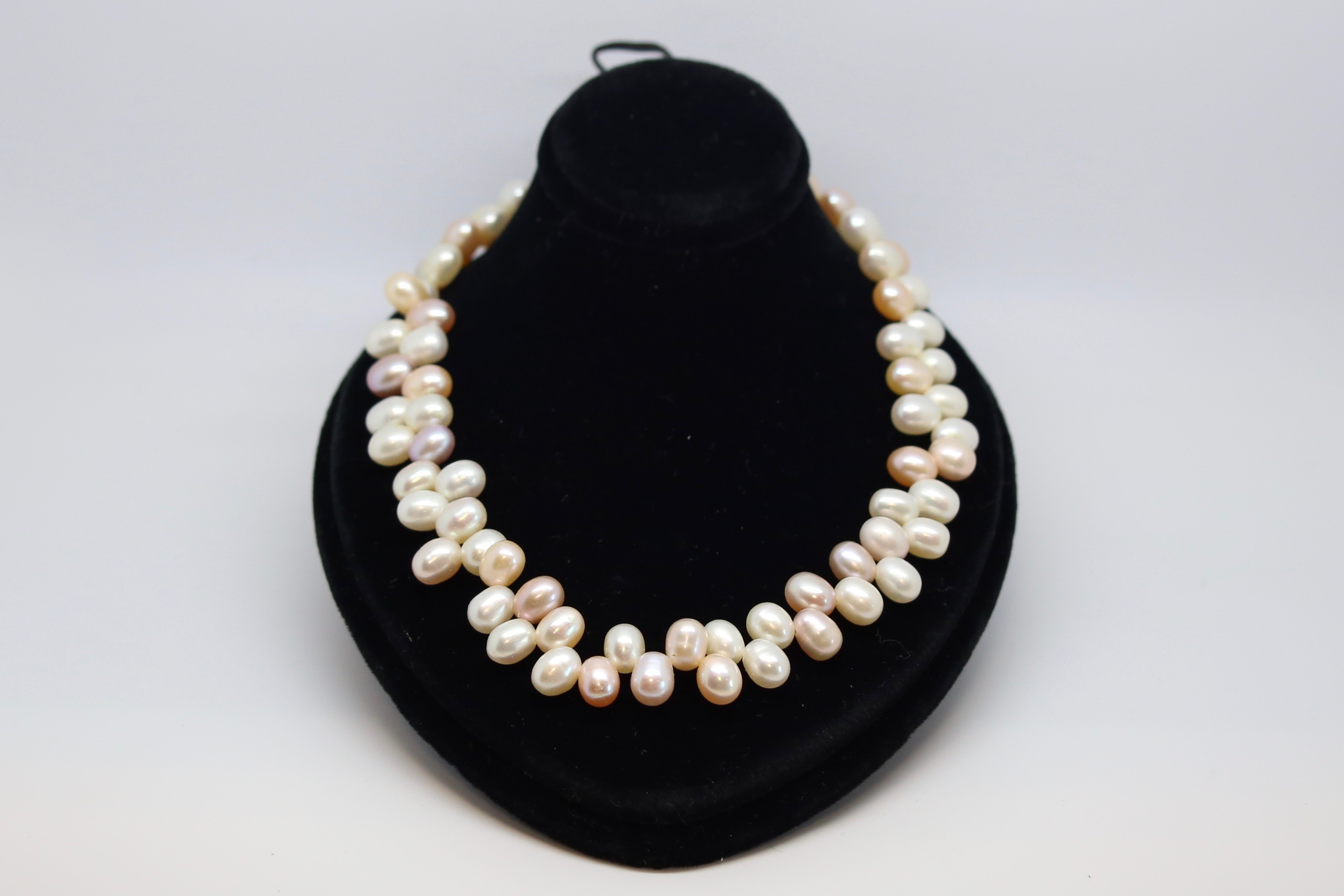 Pearl necklace, set with oval shaped pink, cream and grey pearls in an unusual design, on a yellow