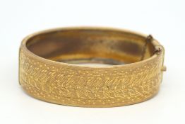 Base metal gold coloured clasp bangle, engraved detail to half the hoop, with safety chain, inside