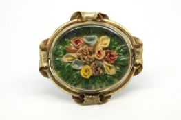 Floral brooch, central carved, painted floral design, set behind a plastic pane, gilt metal border