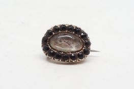 Small Georgian mourning brooch, central oval hair compartment, surrounded by round cut garnets,