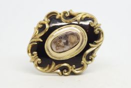 Victorian mourning brooch, central oval hair compartment, within a black enamelled and scrolling