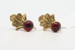 A pair of red stone earrings, round cabochon cut red stone, set below a fan of yellow metal, screw