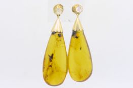 A pair of amber and diamond drop earrings, tear drop shaped amber, suspended from an old cut diamond