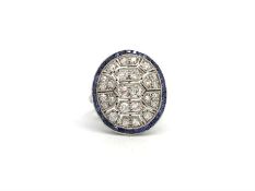 An Art Deco sapphire and diamond panel ring in white metal. The geometric oval panel studded with