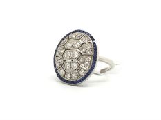 An Art Deco sapphire and diamond panel ring in white metal. The geometric oval panel studded with