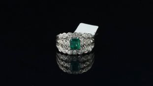 Emerald and diamond ring, central step cut emerald with round brilliant cut diamond detail, in white