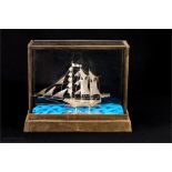 A silver filagree worked model ship in a glass case.