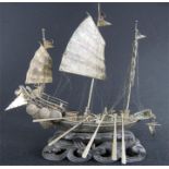 A 19th century Chinese silver junk boat on stand, carved as waves, including six removable oars.