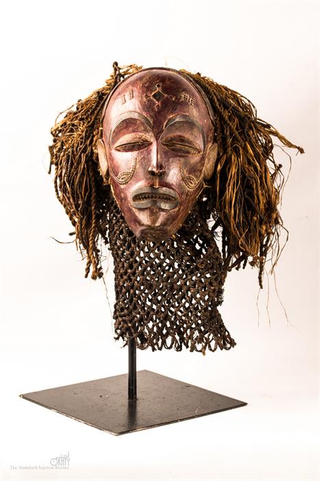 A Chokwe tribal mask, stained colour to the face, and raised on a bespoke metal stand.