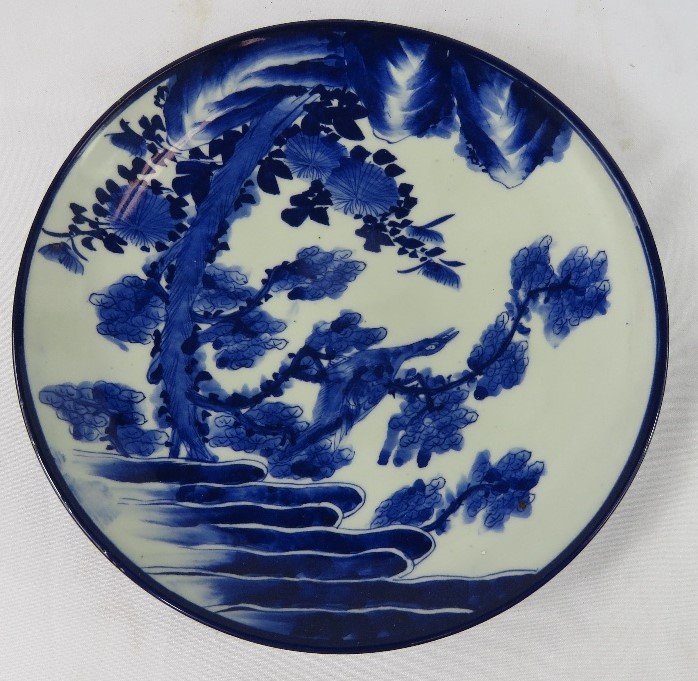 A Japanese wall plate, early 20th century, blue and white depicting birds, rocks, foliage.