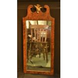 A walnut veneered wall mirror, with gilt crest motif flanked by scrolls, the original mirror