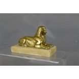 A brass sphinx on a white marble plinth.