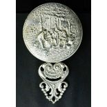 A white metal hand mirror, embossed with farm workers, 11cm high.