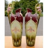 A pair of majolica vases, modelled with daffodil and iris handles, with a maroon ground, 56cm high.