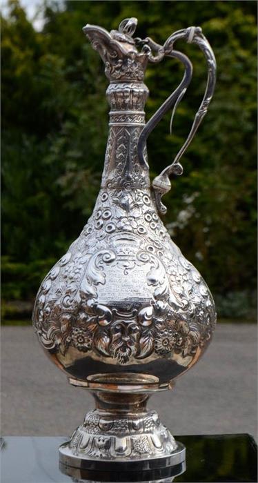 A silver claret jug, embossed with floral decoration, with presentation inscription to the front,