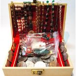 Various coins, un-mounted gems and other items in a cream jewel case.
