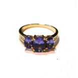 Tanzanite three-stone ring with diamond-set shoulders in 18ct gold.