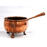 Arts & Crafts copper pan with folded rim, the scroll feet with foliate terminals.