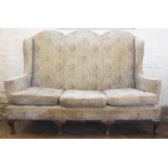 An early 20th century camel back top wing back settee, with floral upholstery on cabriole legs,