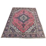 A Persian Tabriz wool carpet, worked with a medallion floral design against a pale red ground,