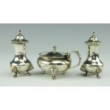 A George V silver three piece condiment set, with gadrooned rims and lion mask scroll feet,