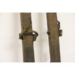 A pair of vintage stained wood alpine skis, each with mounted leather foot locks,
