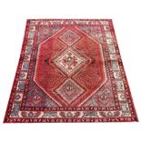 A Persian Shiraz wool rug, worked with three lozenges against a red ground,