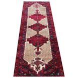 A full pile Persian wool runner, worked with three red geometric gulls against a beige ground,