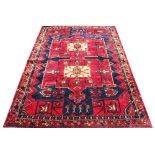 A Hamadan wool carpet, worked with a design of two lozenges, against a red ground,