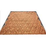 A quilted bed cover, with gold and red floral pattern and serpentine edge,