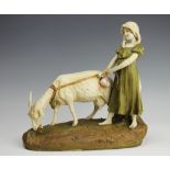 A Royal Dux porcelain figure of a young girl and goat standing on a grassy verge, circa 1905,