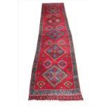 A Persian hand woven wool runner, worked with five medallions against a red ground,