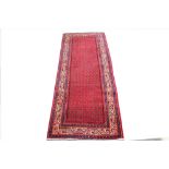 A Persian hand woven wool runner, worked with an all over Sarouk design against a red ground,