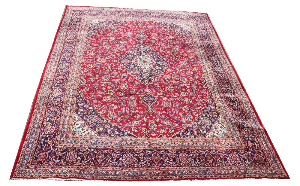 A large Kashan wool carpet, worked with an all over foliate design against a red and blue ground,