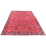 A large Persian Meshad wool carpet, worked with an all over foliate design against a red ground,