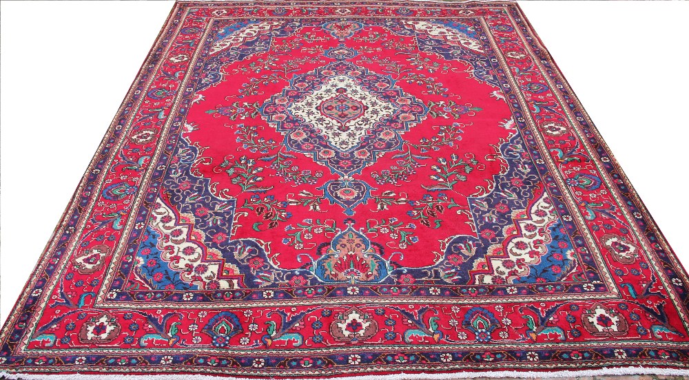 A large hand woven wool Persian Tabriz carpet, worked with floral sprays against a red ground,