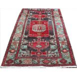 A hand woven wool Persian Hamadan rug, worked with a geometric red panel against a dark ground,