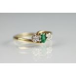 An emerald and diamond cross-over ring, the central emerald flanked by two diamonds,