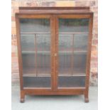 A 1920's oak two door display cabinet, with glazed doors, on scroll legs,