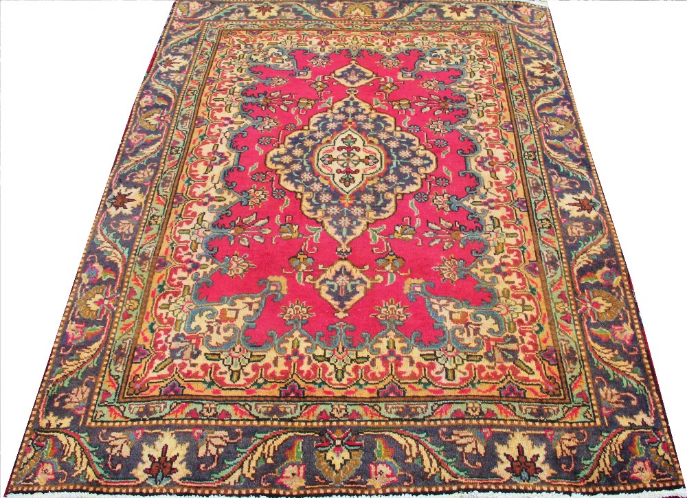 A hand woven wool Persian Tabriz rug, worked with a bold floral design against a red ground,