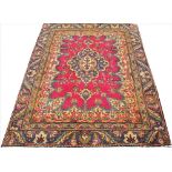 A hand woven wool Persian Tabriz rug, worked with a bold floral design against a red ground,