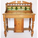 A Victorian pine wash stand, the back inset with five bright floral tiles, above a cupboard door,