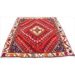 A hand woven wool Persian Qashquai rug, worked with a geometric design against a red ground,